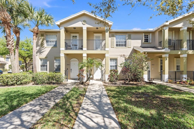 view of front of house with a balcony, stucco siding, and a front yard