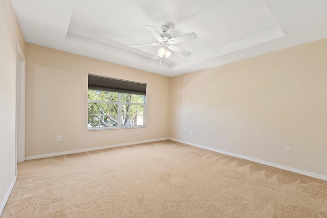 empty room with light colored carpet, baseboards, a tray ceiling, and ceiling fan