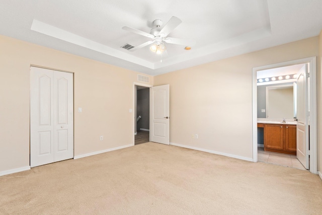 unfurnished bedroom featuring visible vents, light carpet, a tray ceiling, connected bathroom, and baseboards