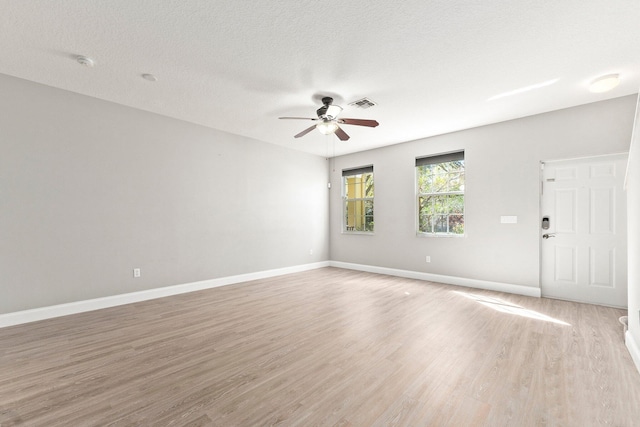 empty room featuring visible vents, baseboards, light wood-style flooring, a textured ceiling, and a ceiling fan