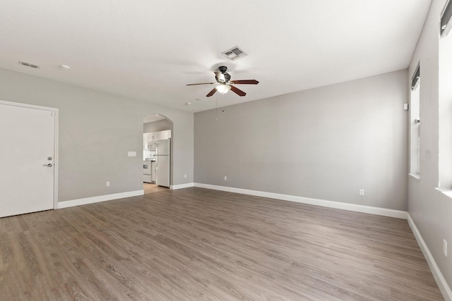 empty room featuring visible vents, arched walkways, light wood-style flooring, and a ceiling fan