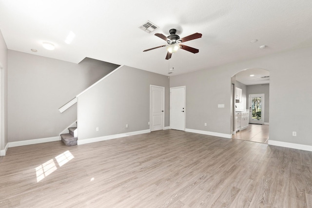 unfurnished living room featuring visible vents, baseboards, arched walkways, stairs, and light wood-style floors