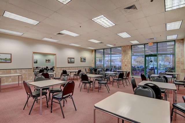 carpeted dining room featuring a wainscoted wall, visible vents, a drop ceiling, and expansive windows