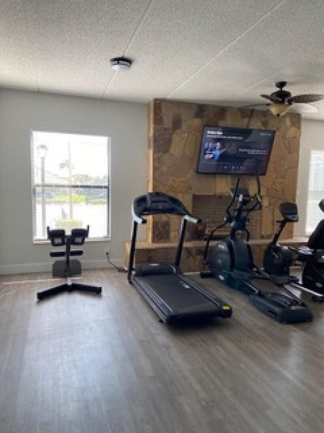 exercise area featuring ceiling fan, a textured ceiling, baseboards, and wood finished floors