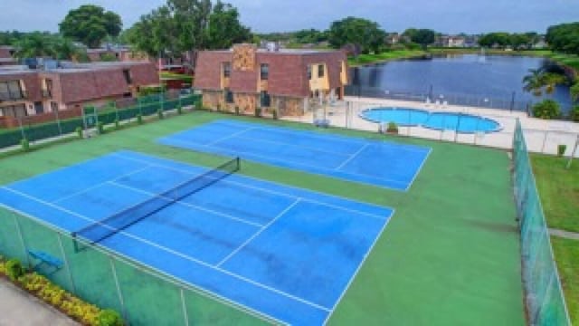 view of tennis court with a water view, a community pool, and fence