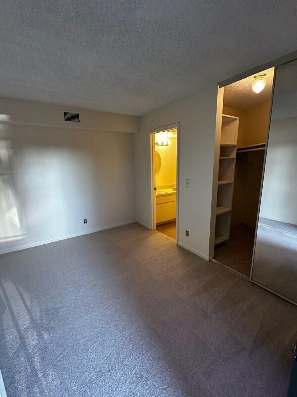 unfurnished bedroom featuring carpet, baseboards, visible vents, a textured ceiling, and connected bathroom