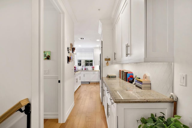 kitchen featuring light stone countertops, visible vents, light wood-style flooring, decorative backsplash, and white cabinets