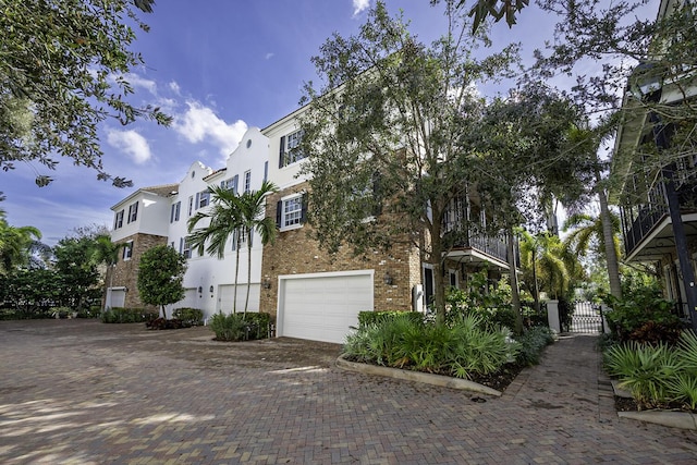 view of front of home with brick siding, stucco siding, decorative driveway, a garage, and a gate