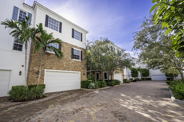 view of front of house with decorative driveway, brick siding, and stucco siding