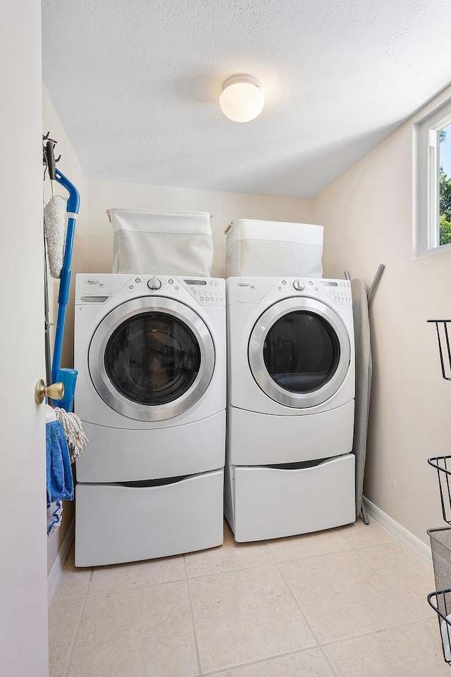 clothes washing area with baseboards, laundry area, separate washer and dryer, a textured ceiling, and tile patterned floors