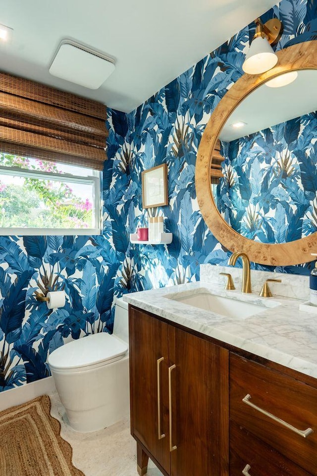 half bathroom with toilet, wallpapered walls, and vanity