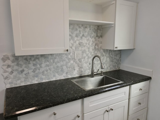 kitchen with a sink, open shelves, backsplash, dark stone counters, and white cabinets