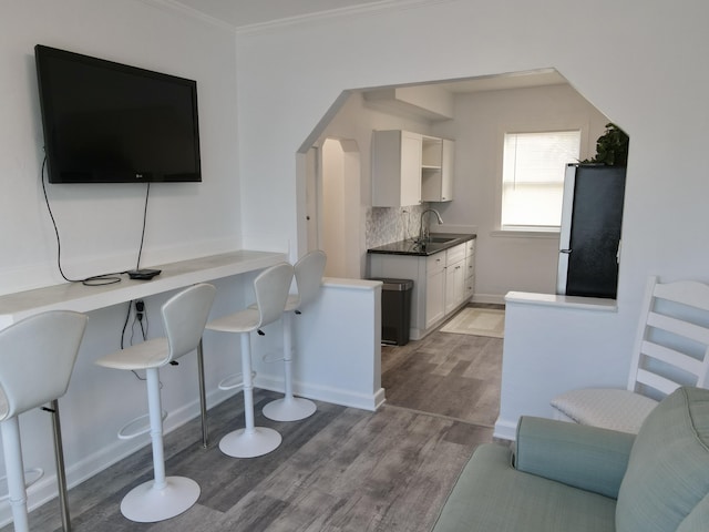 kitchen featuring decorative backsplash, freestanding refrigerator, wood finished floors, arched walkways, and a sink