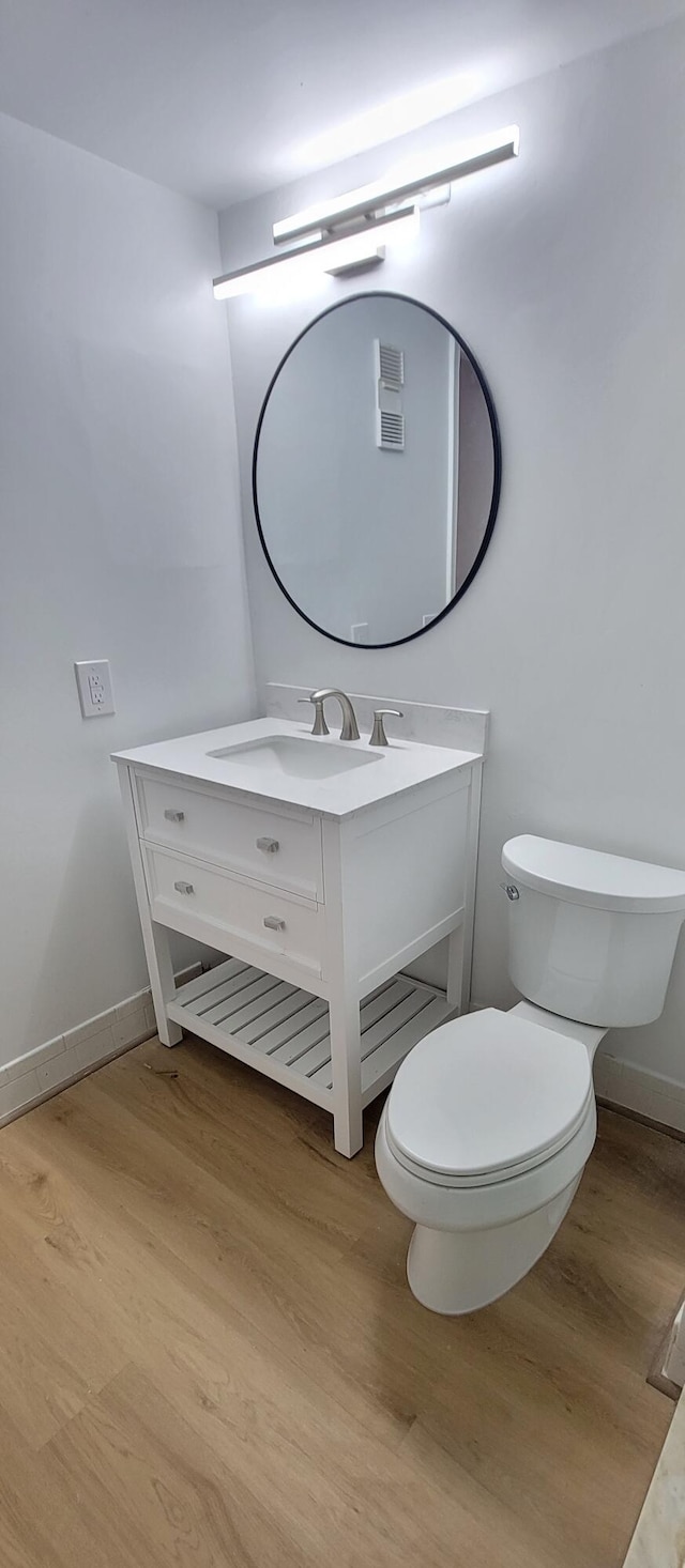 bathroom featuring baseboards, toilet, wood finished floors, and vanity