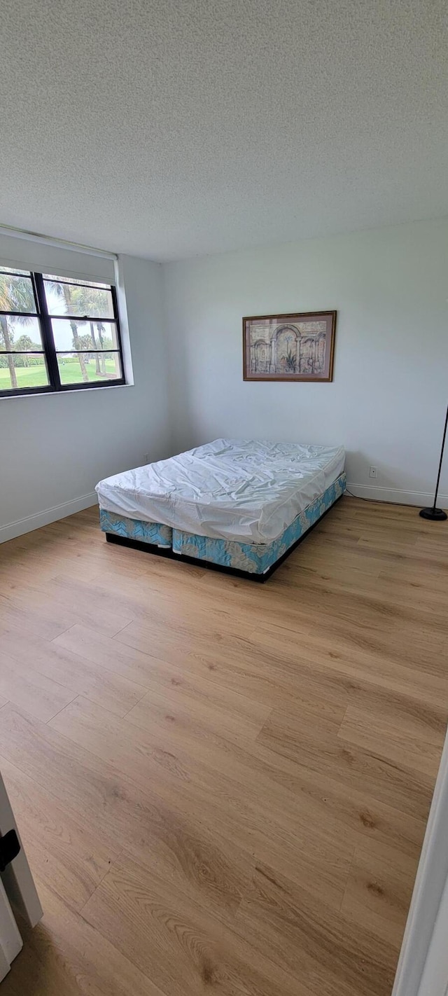 unfurnished bedroom with a textured ceiling, baseboards, and wood finished floors