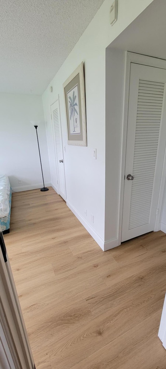 hall featuring light wood-style floors, baseboards, and a textured ceiling