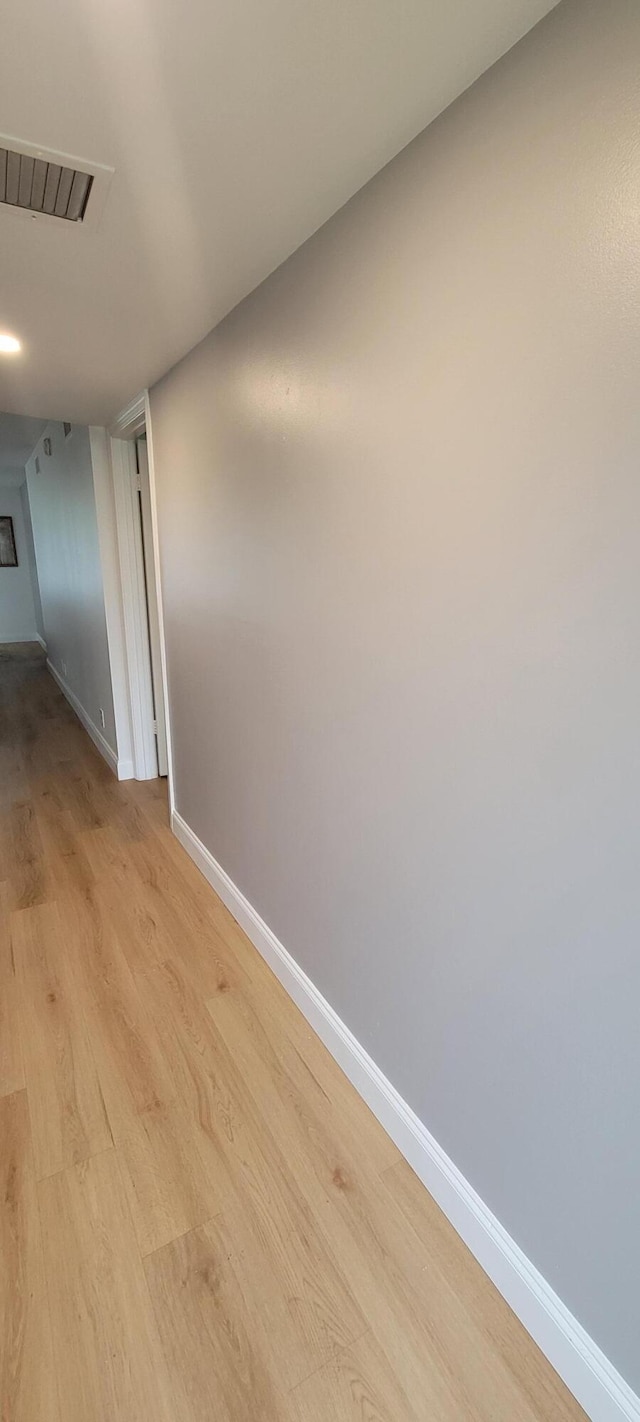 corridor with visible vents, light wood-type flooring, and baseboards