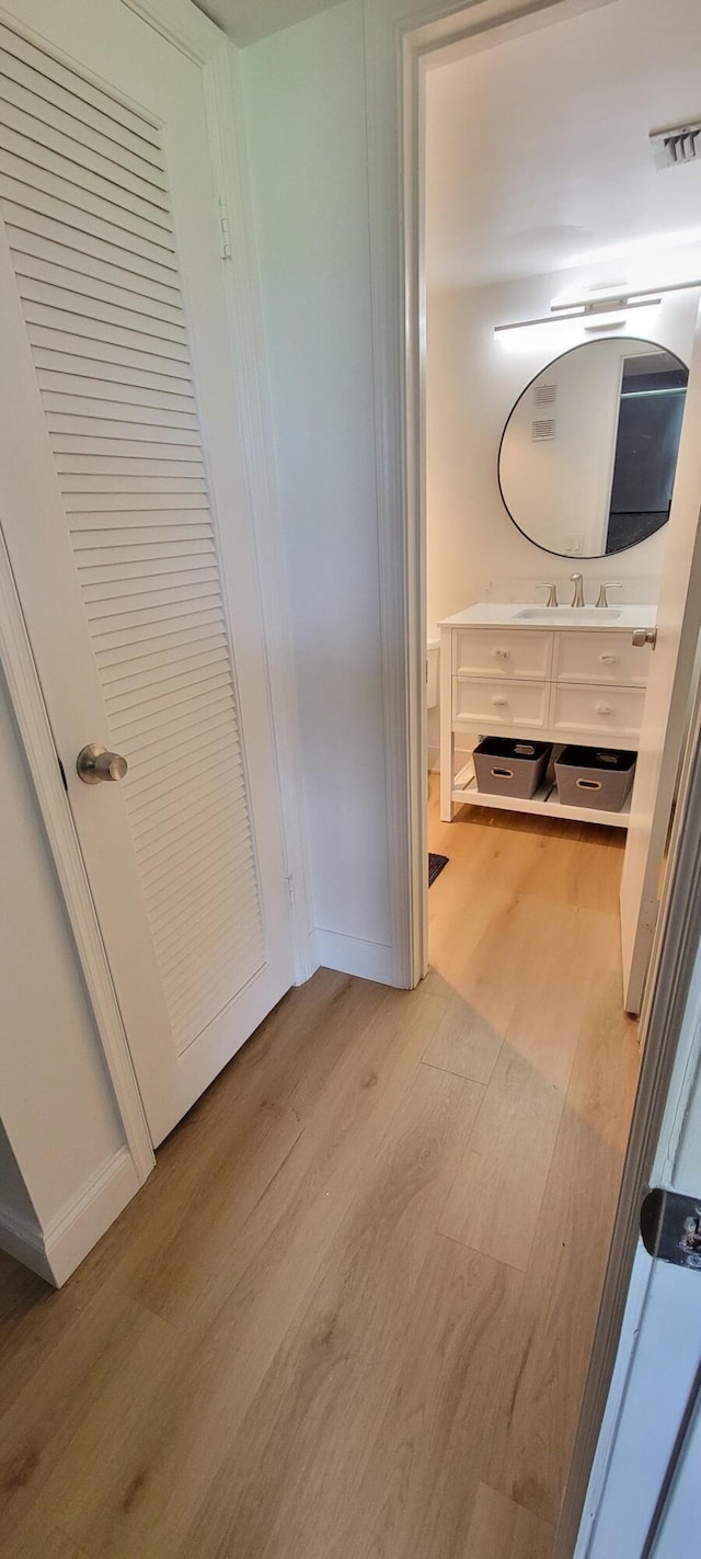 hallway featuring visible vents, light wood-type flooring, baseboards, and a sink