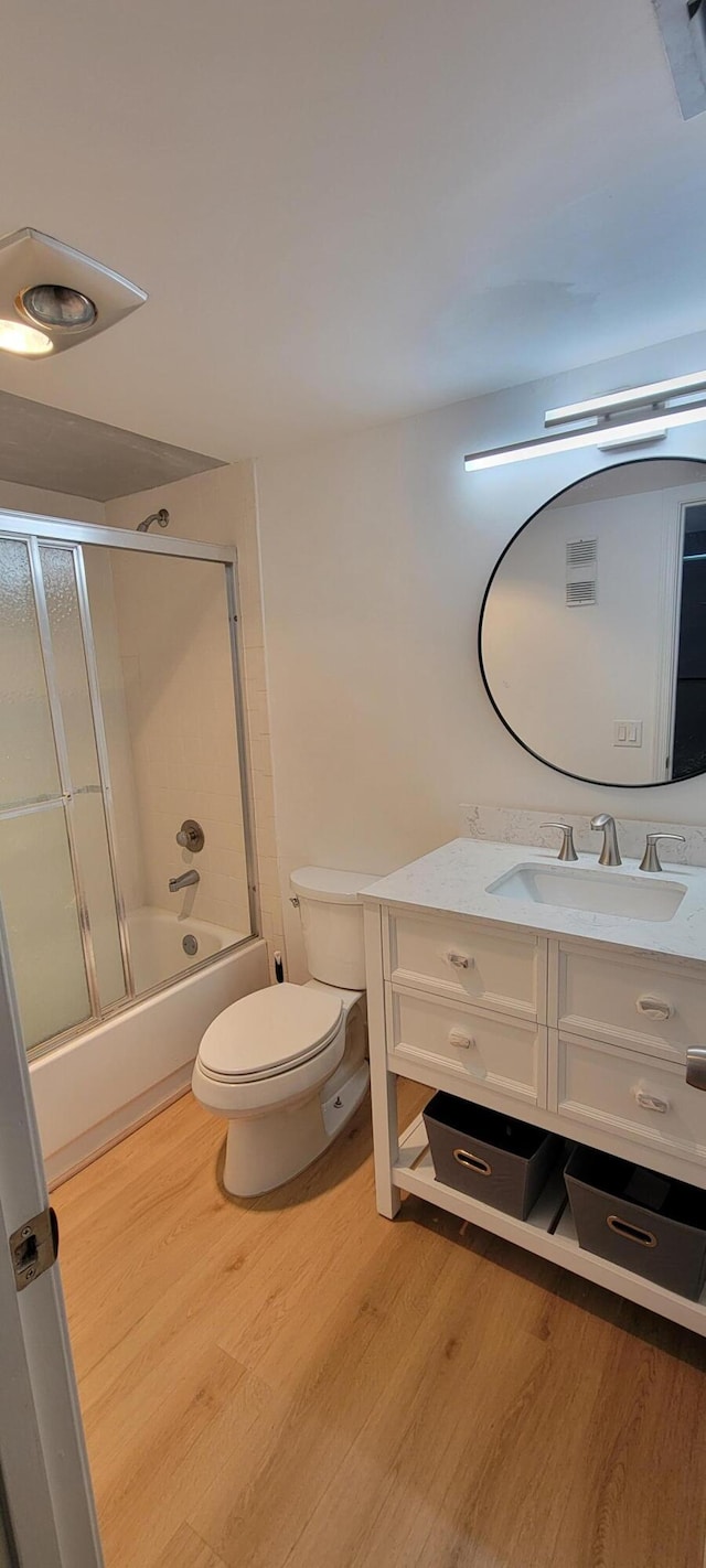 bathroom featuring combined bath / shower with glass door, toilet, wood finished floors, and vanity