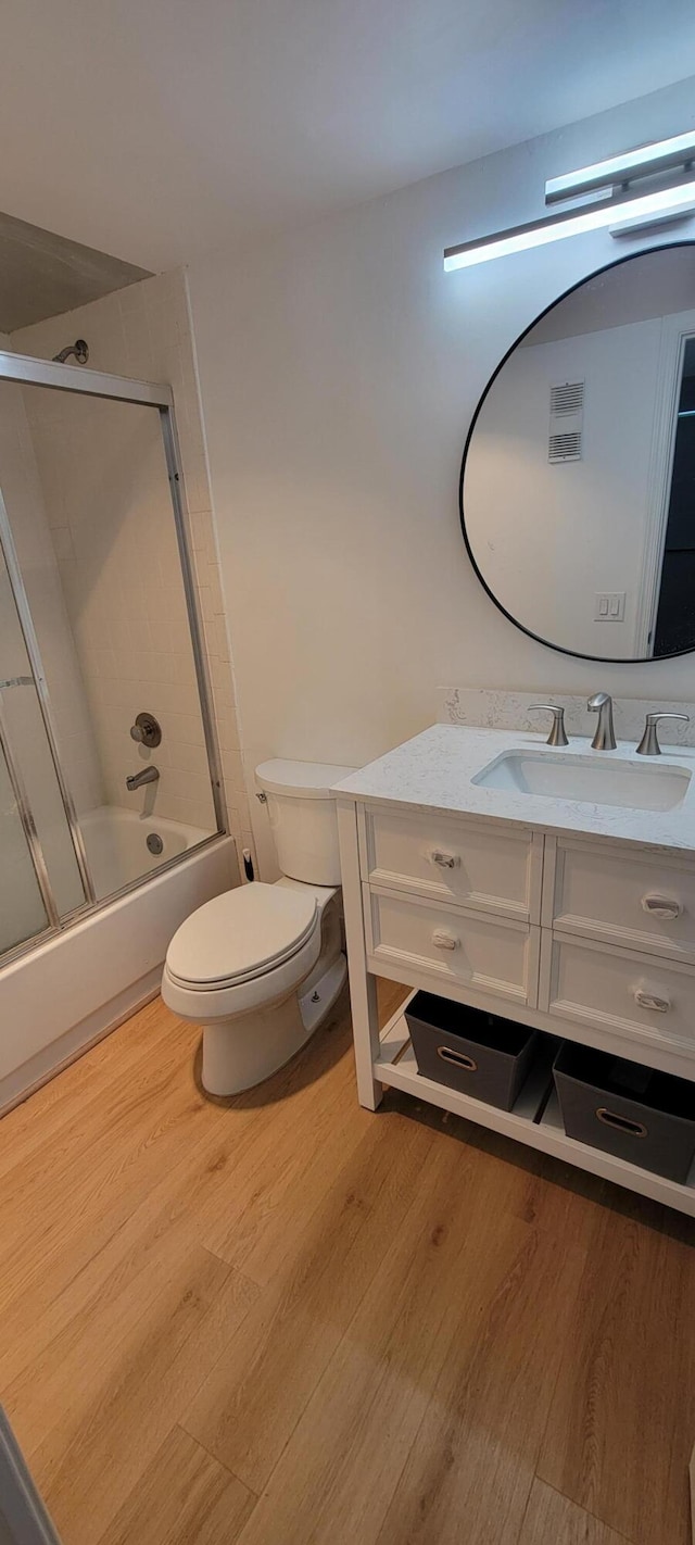 bathroom with vanity, toilet, wood finished floors, and combined bath / shower with glass door