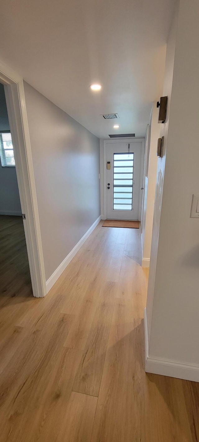 corridor with light wood-style flooring, visible vents, baseboards, and a wealth of natural light