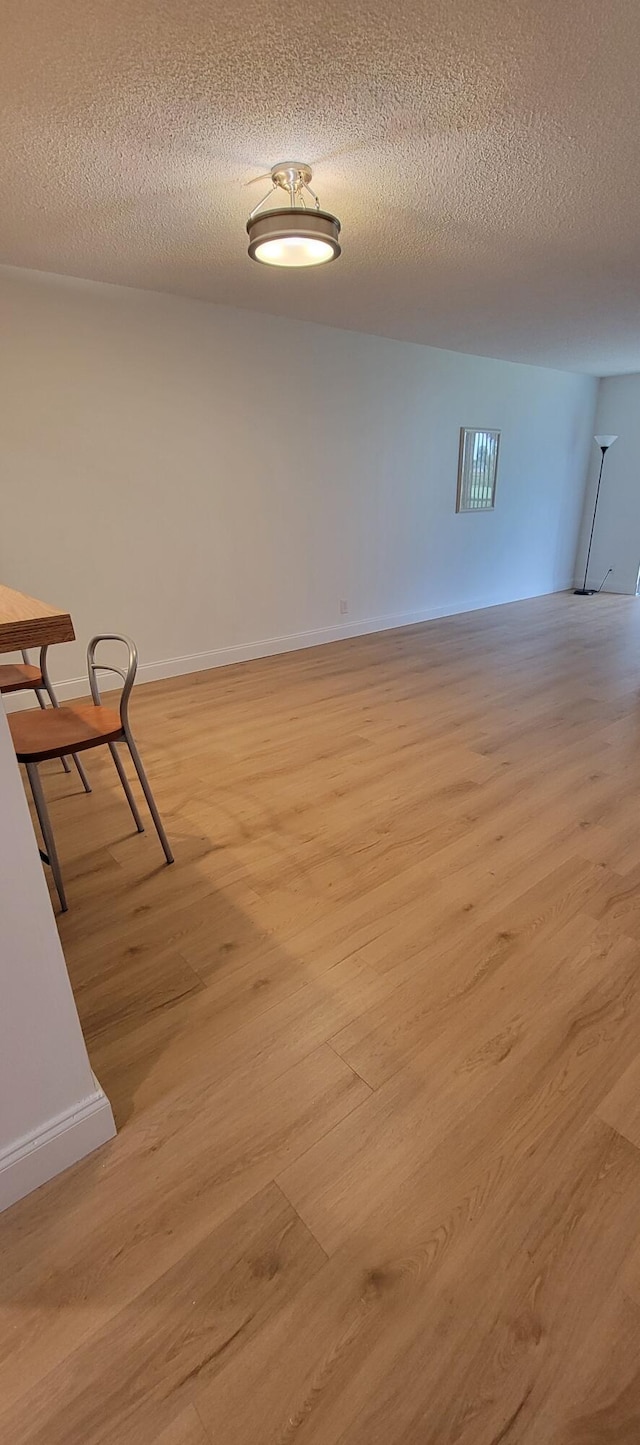 hallway with light wood-type flooring, baseboards, and a textured ceiling