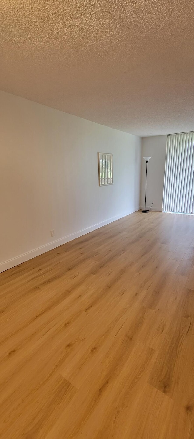 spare room featuring baseboards, light wood-type flooring, and a textured ceiling