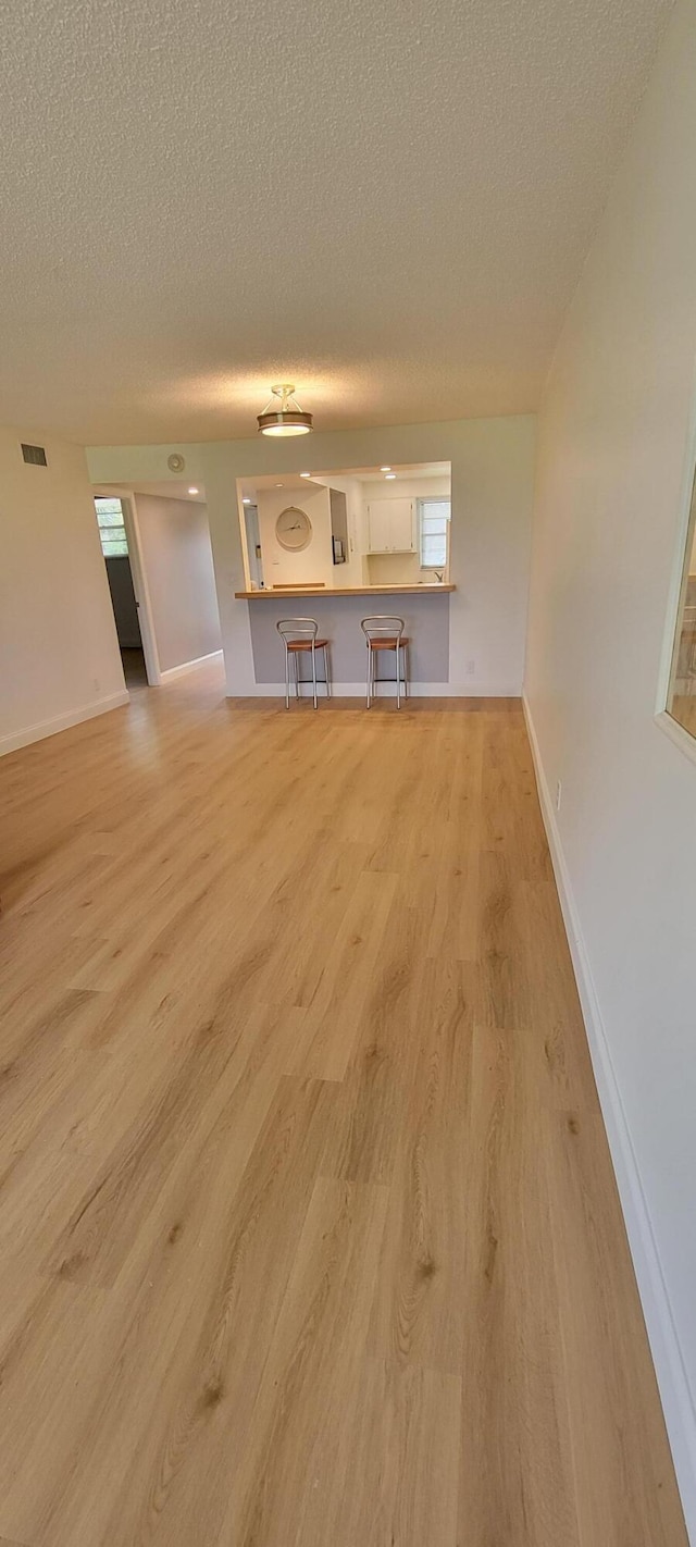 unfurnished living room featuring visible vents, baseboards, light wood-style floors, and a textured ceiling