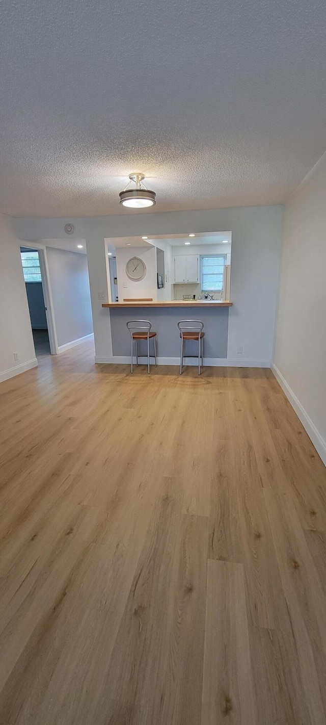 unfurnished living room with baseboards, plenty of natural light, a textured ceiling, and wood finished floors