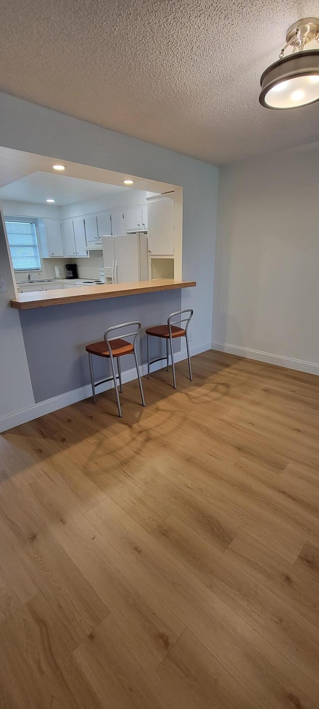 kitchen featuring baseboards, a breakfast bar area, white refrigerator with ice dispenser, wood finished floors, and white cabinetry