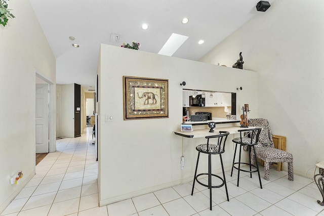 kitchen with high vaulted ceiling, a skylight, a breakfast bar area, light countertops, and light tile patterned floors