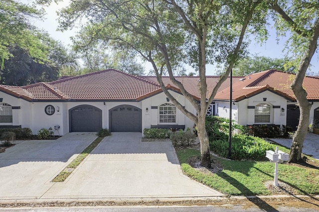 mediterranean / spanish-style home featuring an attached garage, a front lawn, a tiled roof, stucco siding, and driveway