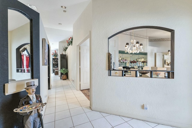 hallway featuring tile patterned floors, visible vents, arched walkways, an inviting chandelier, and a textured wall