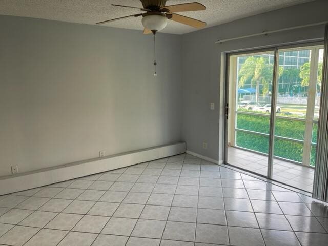 empty room with a ceiling fan, a textured ceiling, light tile patterned floors, a baseboard radiator, and baseboards