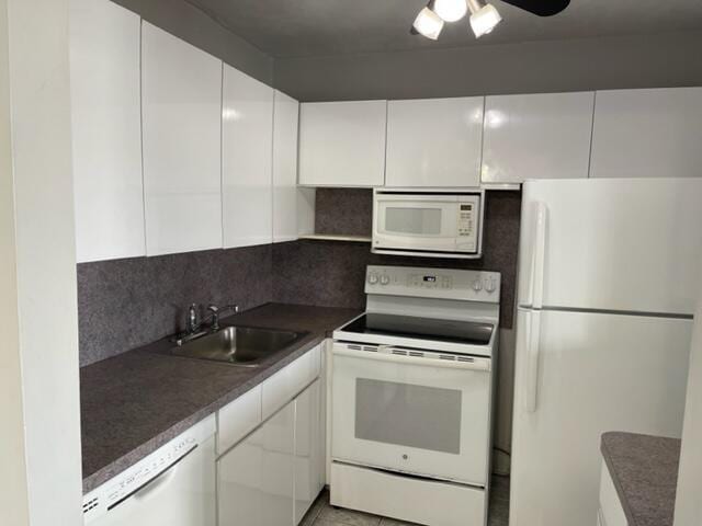 kitchen with a sink, dark countertops, white appliances, white cabinets, and decorative backsplash