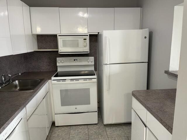 kitchen with dark countertops, backsplash, white appliances, white cabinetry, and a sink