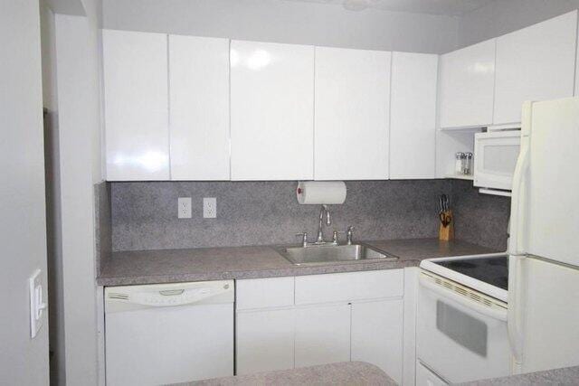 kitchen featuring white appliances, white cabinets, tasteful backsplash, and a sink