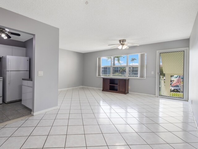 empty room with light tile patterned floors, a ceiling fan, baseboards, and a textured ceiling