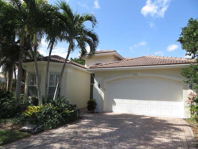 mediterranean / spanish home featuring a tiled roof, stucco siding, an attached garage, and decorative driveway