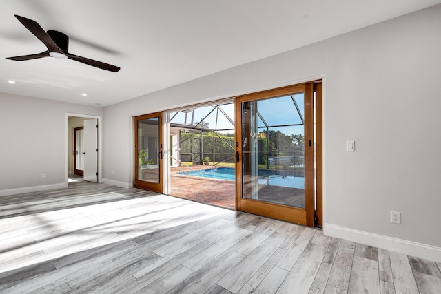 empty room featuring baseboards, light wood finished floors, a ceiling fan, and a sunroom