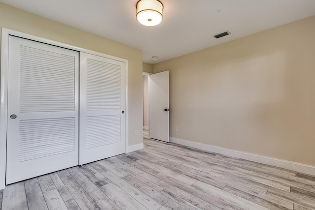 unfurnished bedroom with wood finished floors, visible vents, a closet, and baseboards