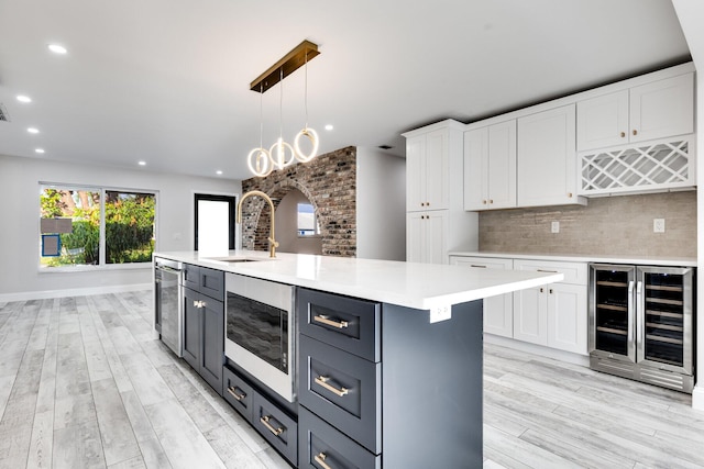 kitchen featuring stainless steel microwave, wine cooler, decorative backsplash, white cabinetry, and a sink