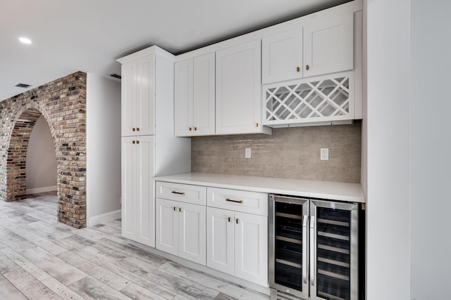 bar with tasteful backsplash, wine cooler, light wood-style flooring, arched walkways, and a bar