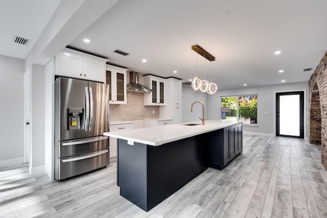 kitchen featuring backsplash, a large island with sink, stainless steel refrigerator with ice dispenser, wall chimney exhaust hood, and a sink