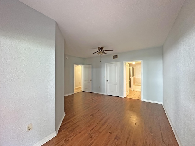 empty room featuring visible vents, a ceiling fan, wood finished floors, baseboards, and a textured wall