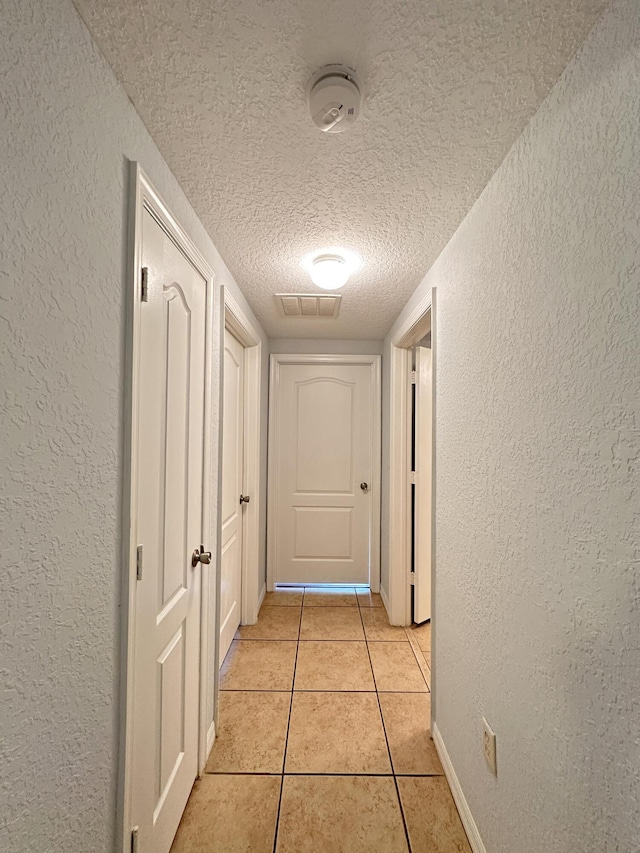 hall featuring light tile patterned flooring, visible vents, a textured ceiling, and a textured wall