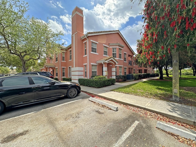 view of front of home with a front lawn, stucco siding, cooling unit, a chimney, and uncovered parking