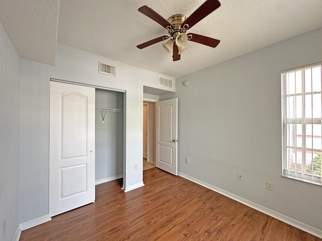 unfurnished bedroom with baseboards, wood finished floors, visible vents, and a textured ceiling