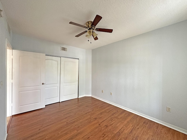 unfurnished bedroom with a closet, a textured ceiling, baseboards, and wood finished floors