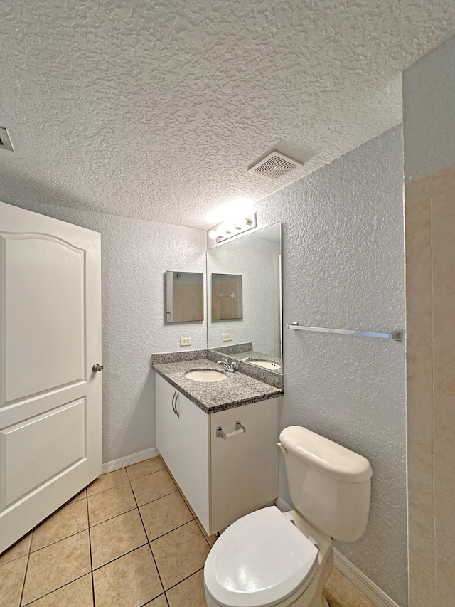 bathroom featuring vanity, tile patterned floors, toilet, and a textured wall